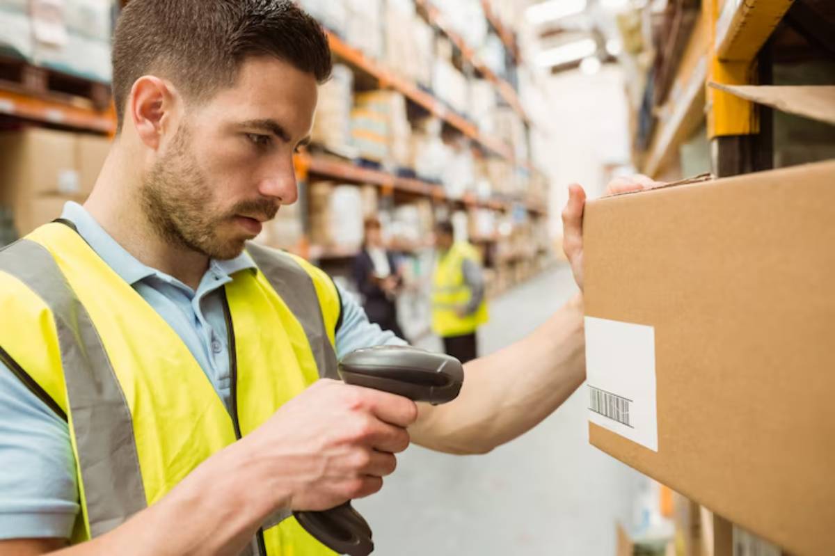 A warehouse worker scans a barcode on a box while surrounded by shelves filled with inventory.