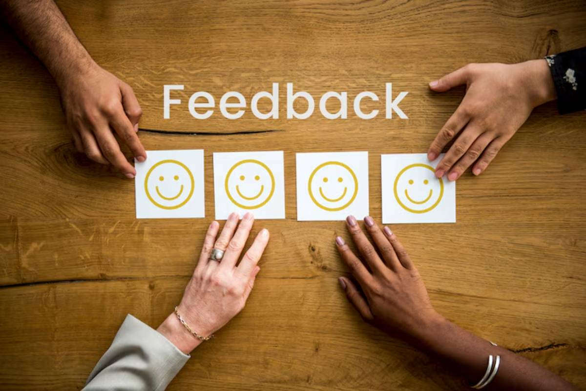 Hands reaching for smiley face rating cards on a wooden table, with the word Feedback displayed above them.