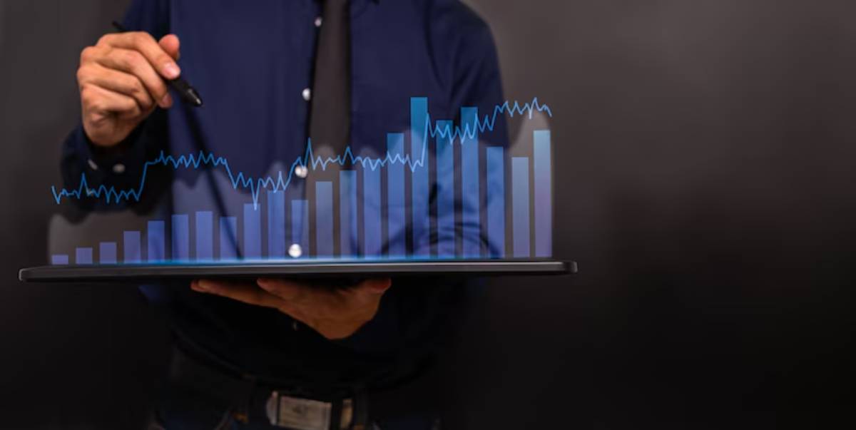 A person in a blue shirt holds a laptop displaying a holographic bar graph, symbolizing data analysis and business growth.