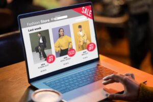 A laptop screen displaying a fashion store sale with three garments, highlighting discounts of 50% and 80%. A coffee cup is nearby.