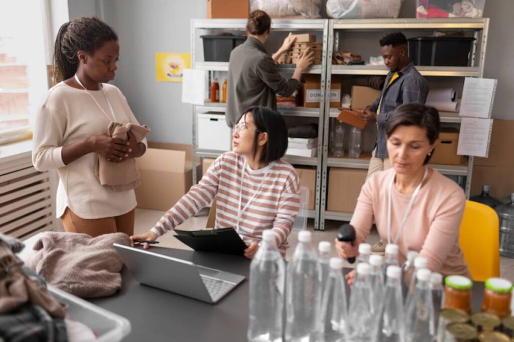 A group of people collaborating in a room filled with donations, laptops, and packed items, focused on their tasks.