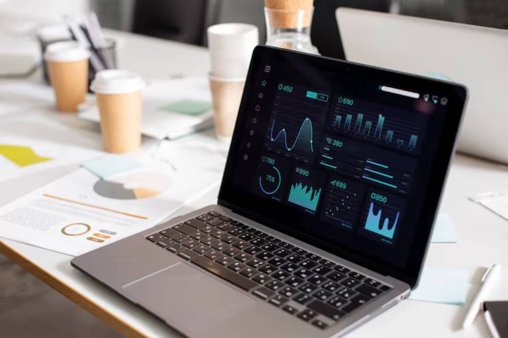 A laptop displays analytics data on a sleek interface, surrounded by coffee cups and documents on a modern office table.