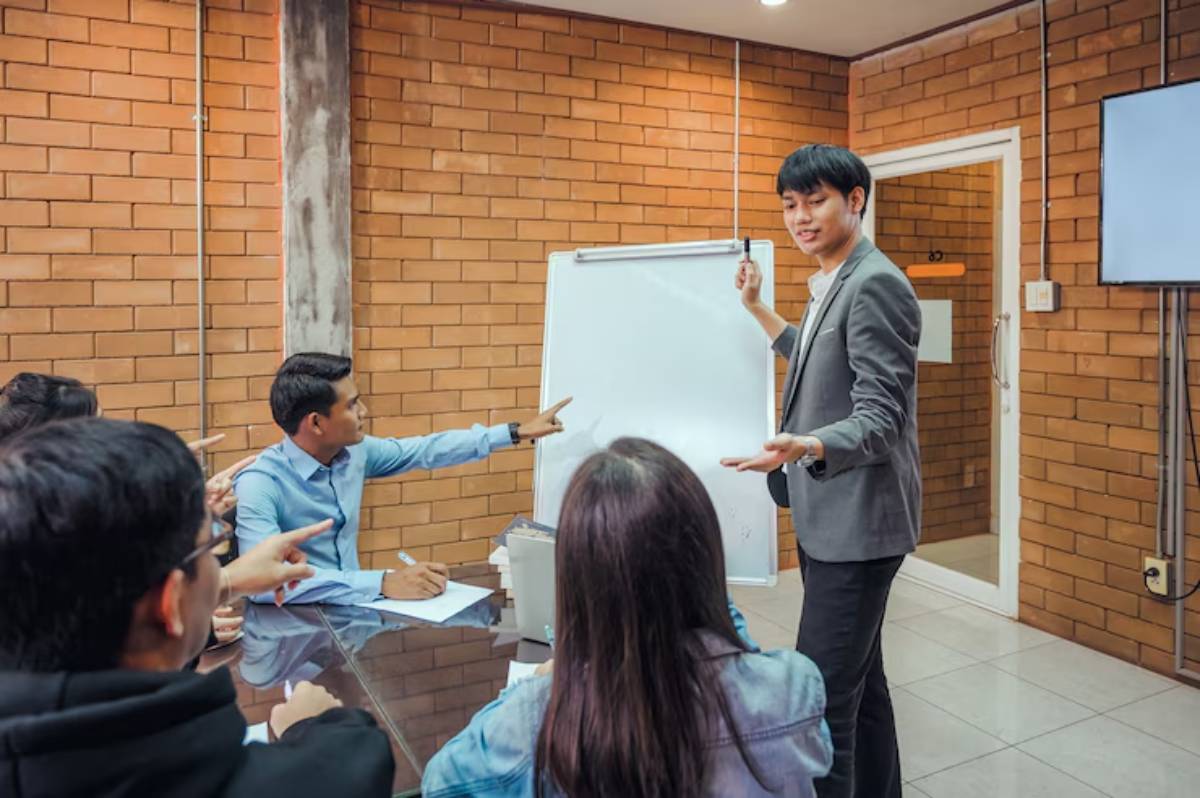 A professional meeting in a modern conference room, with participants engaged in discussion around a whiteboard presentation.