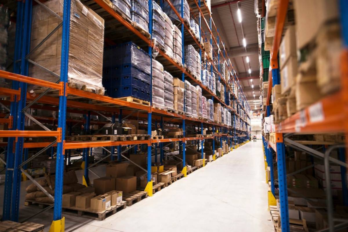 A spacious warehouse aisle lined with tall shelves full of boxes and pallets, showcasing organized storage.
