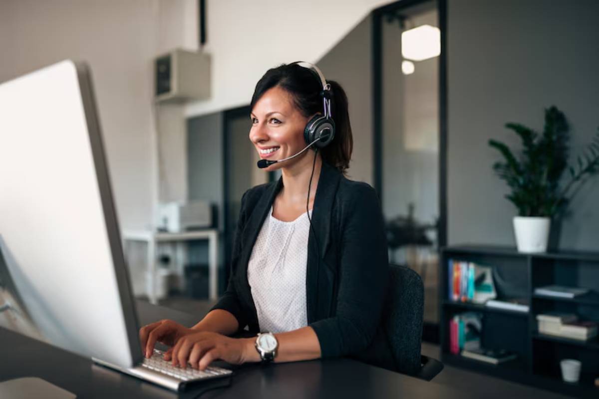 A person wearing headphones is working at a desk with a large computer screen in a modern office setting.