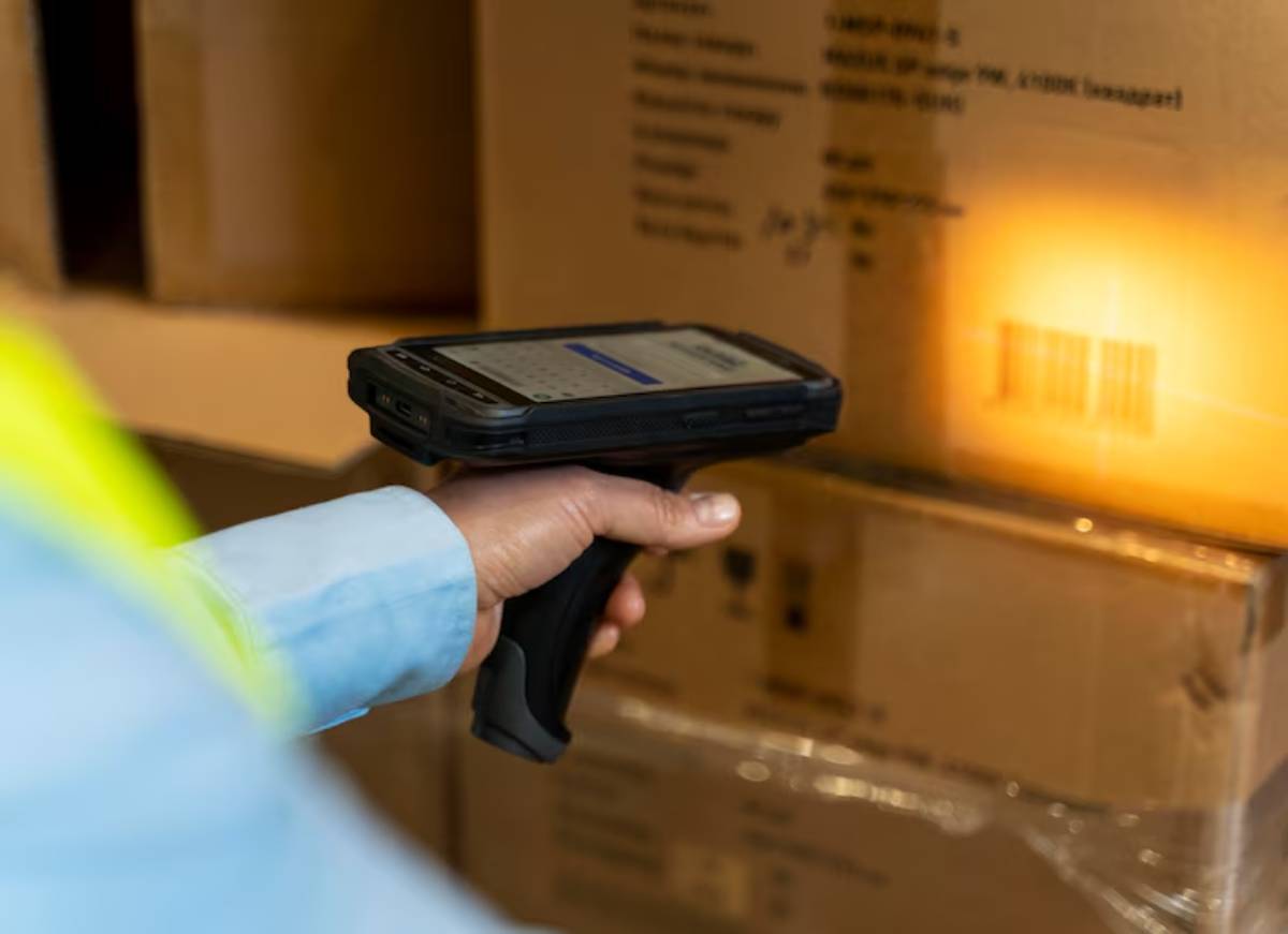 A person scans a barcode on a cardboard box using a handheld device in a warehouse setting.