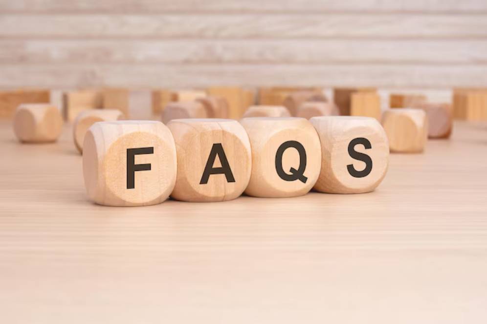 Wooden blocks spelling FAQS on a light wooden surface, with more blocks scattered in the background.